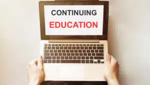 person studying to become an employing broker holding a laptop with "continuing education" on its screen