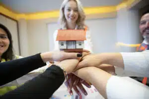 employing broker and her team gathered around a table with their hands stacked on top of each other with a model house on top